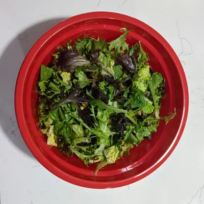 a red bowl filled with lettuce on top of a table