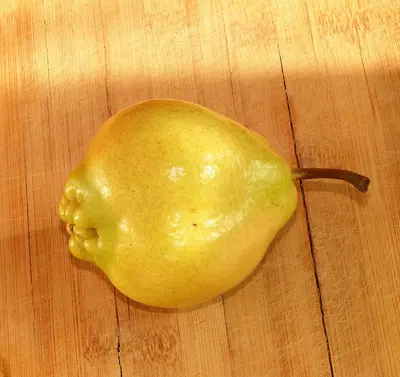 A yellow pear sitting on top of a wooden cutting board